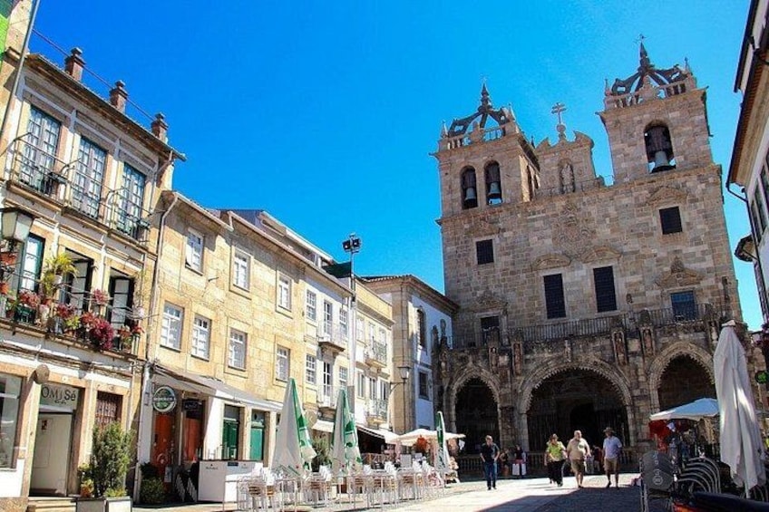 A historic stone building with two towers, a paved square with outdoor seating, and a clear blue sky. 3