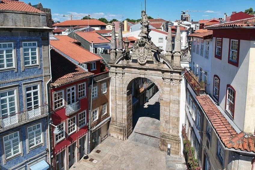 A historic stone archway in a European town, surrounded by colorful buildings with red-tiled roofs. 4