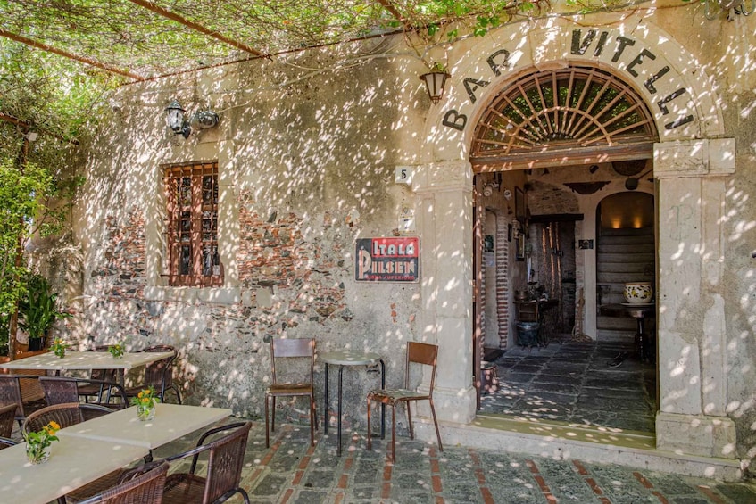 An outdoor café with rustic stone walls, wooden furniture, and a sign reading "Bar Vitellet." 3