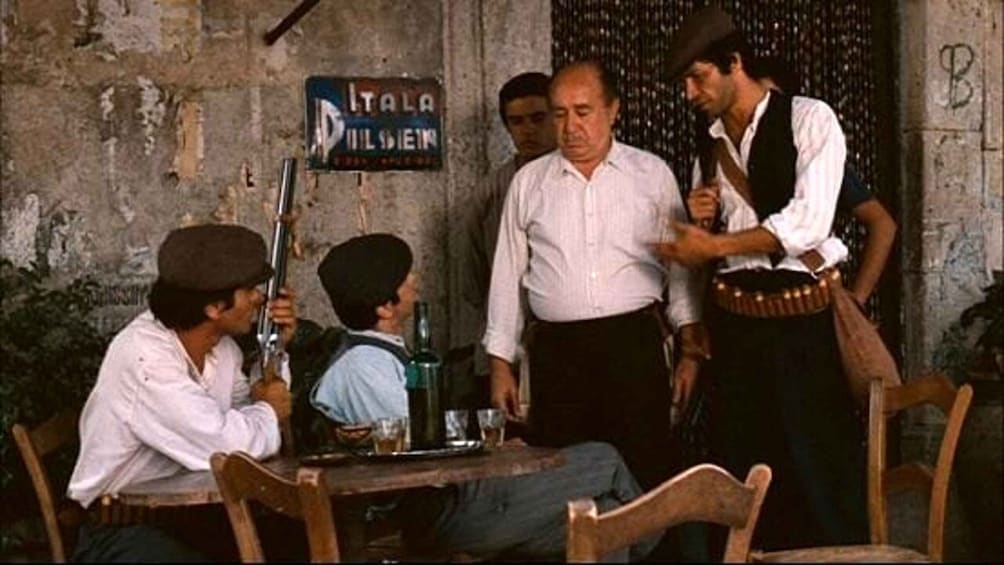 A group of people in a rustic setting with a sign that reads "ITALA PILOSEIN". 1