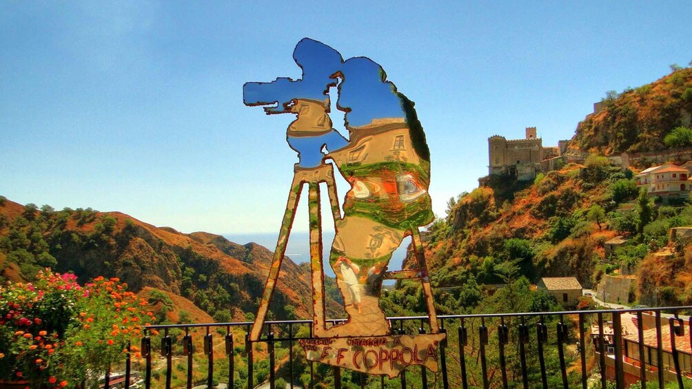 A large sculpture of a person on a tripod in a mountainous landscape with a castle in the background. 2