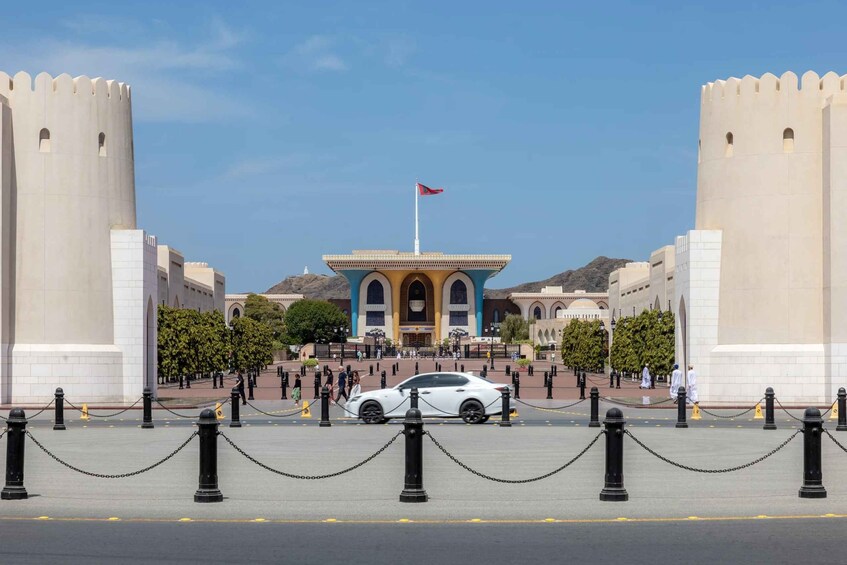A historic gate with a flag, surrounded by a chain barrier and a white car in the foreground. 5