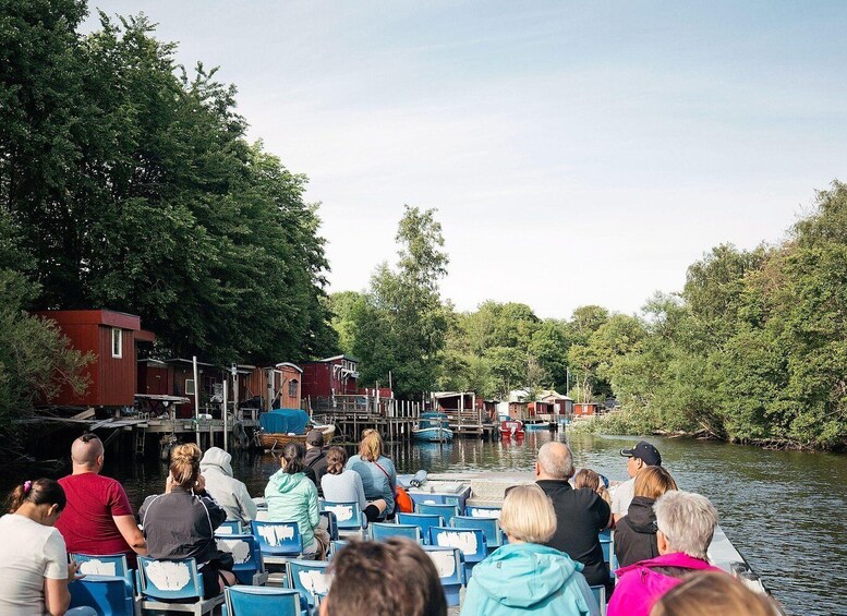 Een groep mensen op een boot, een steiger met huizen en een rivier omringd door bomen. 3