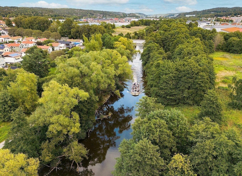 Een rivier meandert door een dichtbegroeid gebied, met huizen aan één kant en een brug in de verte. 4
