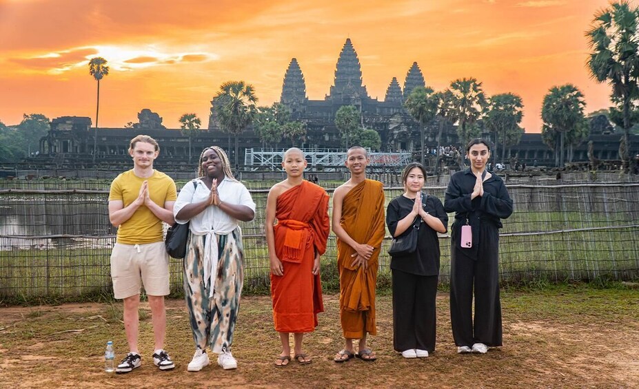 A group of people standing in front of Angkor Wat temple at sunset. 1