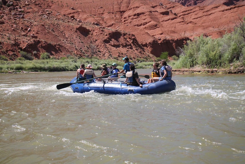A group of people rafting on a river with red rock cliffs in the background. 5