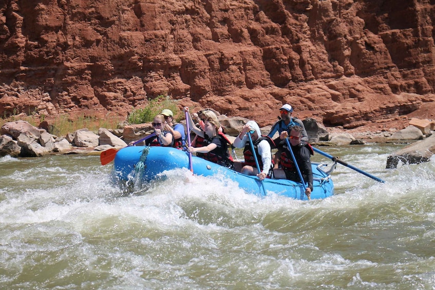A group of people rafting on a river with a red rock canyon in the background. 2