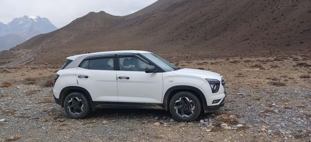 A white SUV parked on a rocky terrain with mountains in the background. 5