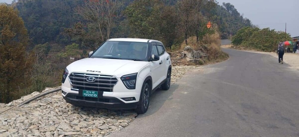 A white SUV parked on a rural road with a rocky embankment and trees in the background. 3