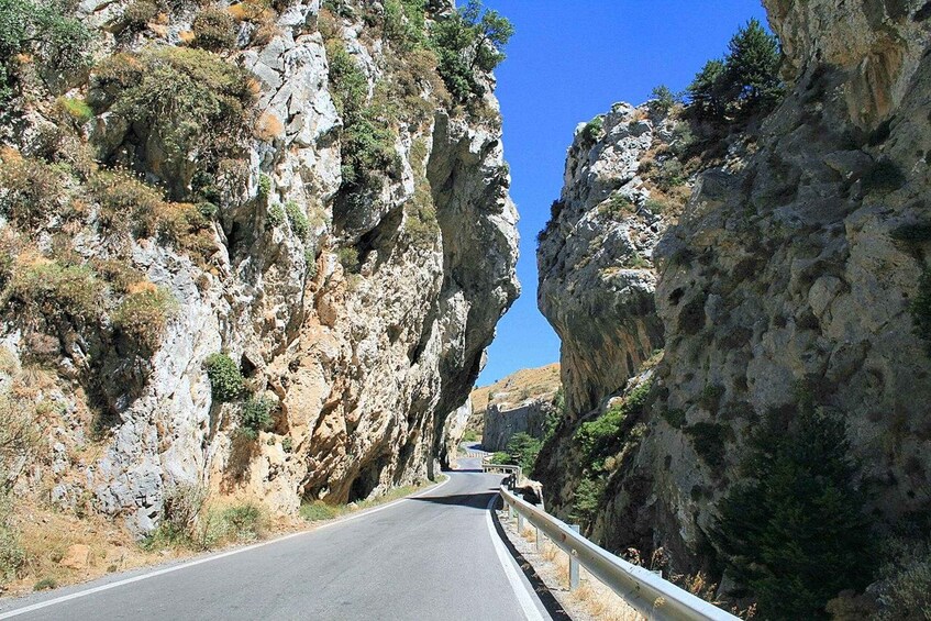 A narrow road flanked by rocky cliffs and sparse vegetation. 1
