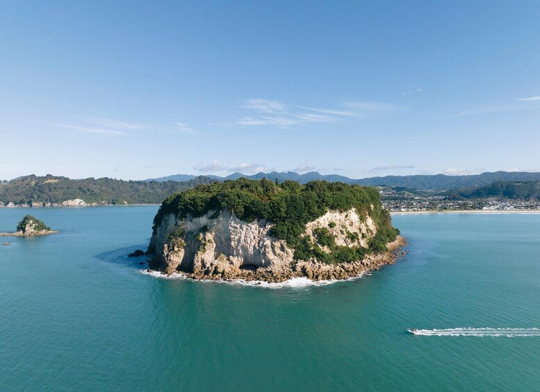 A large island with a rocky coastline surrounded by calm blue waters and distant mountains. 4
