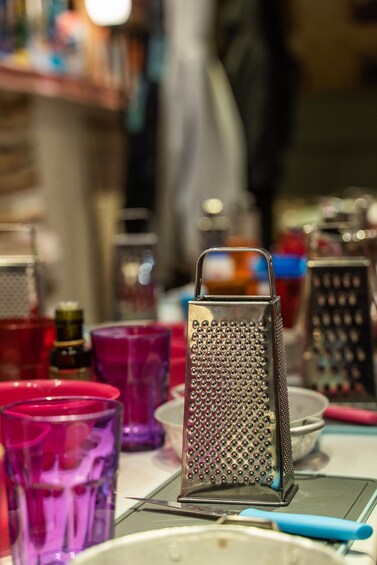 A metal grater on a table with colorful glass containers and a blue pen. 1