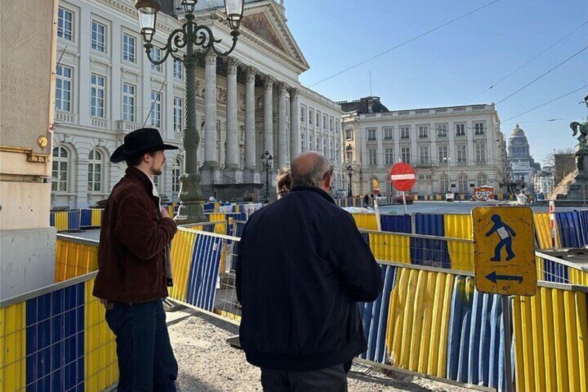 A man in a brown jacket and black hat standing near a barricade with a pedestrian sign. 2