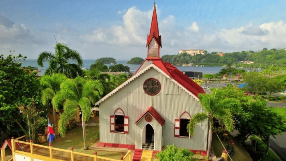 A church with a red roof and white walls, surrounded by greenery and a body of water. 2