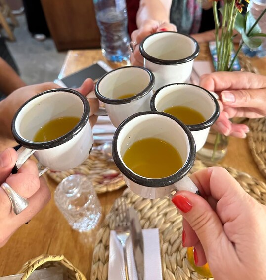 A group of people holding white mugs with black rims, filled with a yellow liquid, likely tea or coffee, at a table. 5