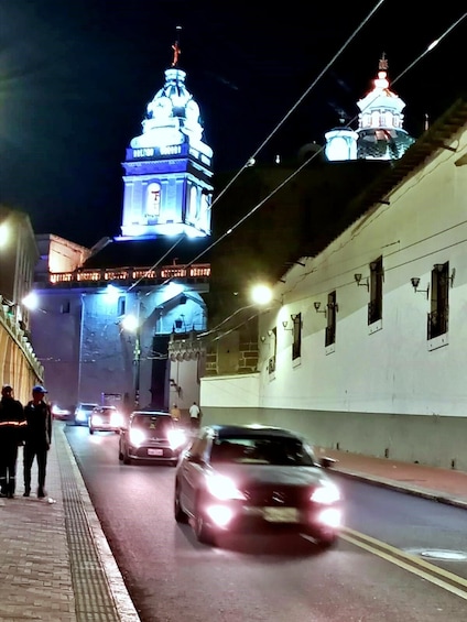A nighttime street scene with illuminated buildings, a domed structure, and vehicles. 3
