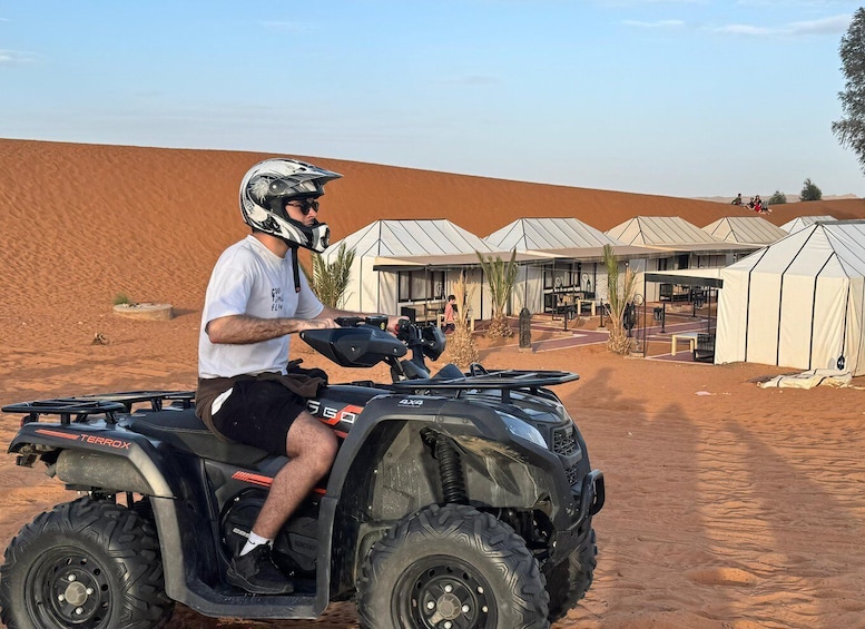 Une personne conduisant un quad noir dans un désert, avec des tentes en arrière-plan. 4