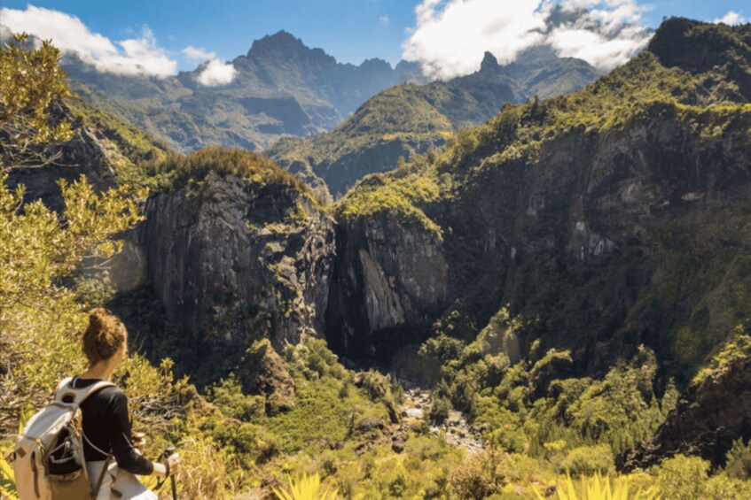 A hiker in a mountainous landscape with dense vegetation and rocky cliffs. 1