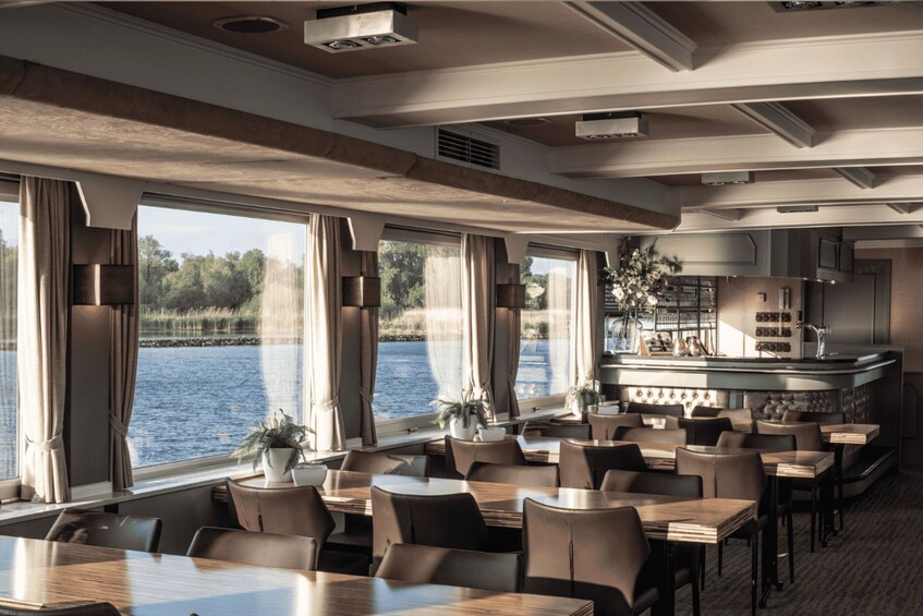 A restaurant with large windows overlooking a body of water, wooden tables and chairs, and a bar area. 5