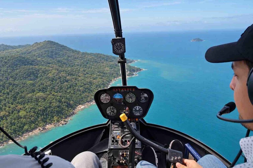 A helicopter cockpit with a view of a coastline and forested hills. 5