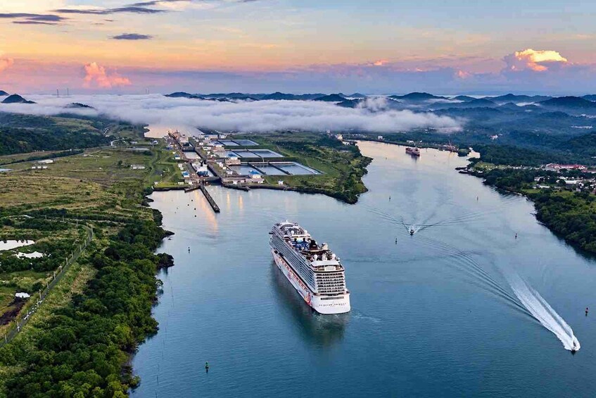 A cruise ship navigating a river with industrial facilities and mountains in the background. 2