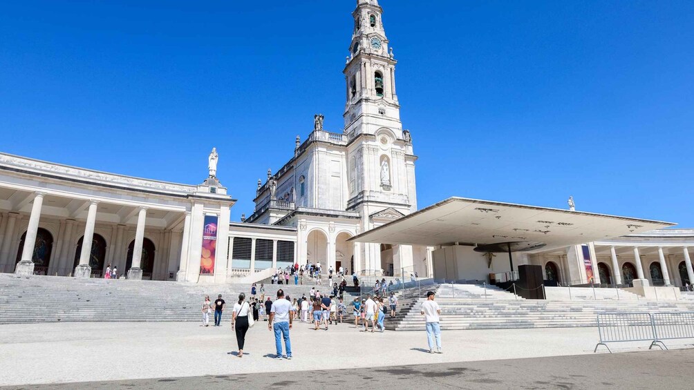 A large public square with a prominent clock tower, steps leading up to a building with classical architecture, and a covered area with columns. 2