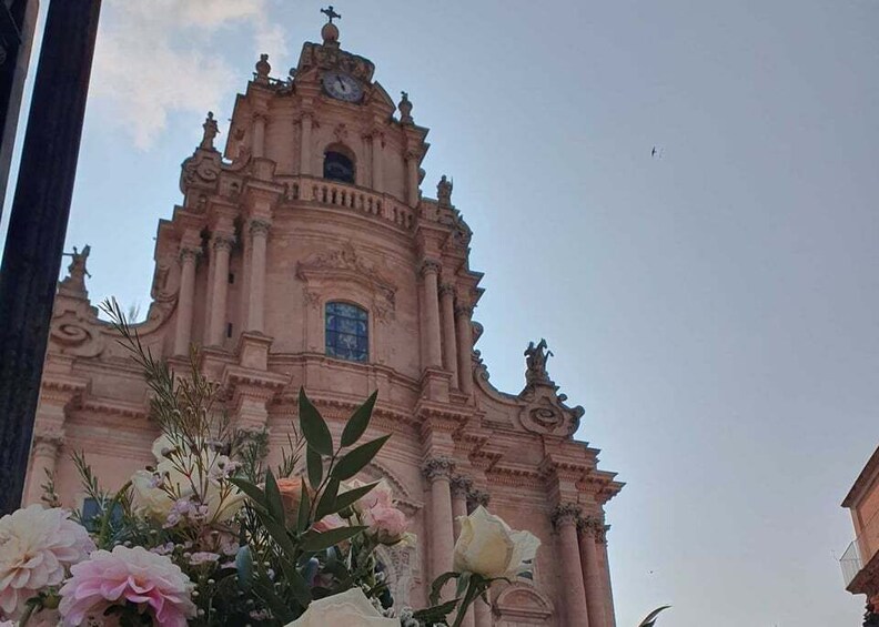 A pink church with a clock tower and a flower arrangement in the foreground. 2