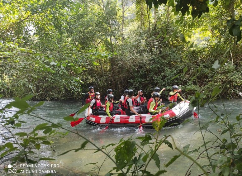 A group of people in a red and white raft navigating a river surrounded by dense greenery. 3