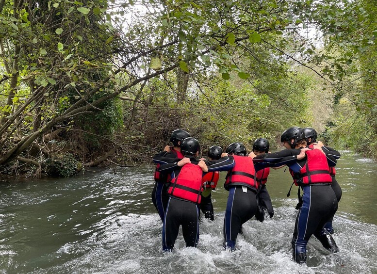 A group of people in life jackets and helmets navigating through a river surrounded by dense foliage. 5