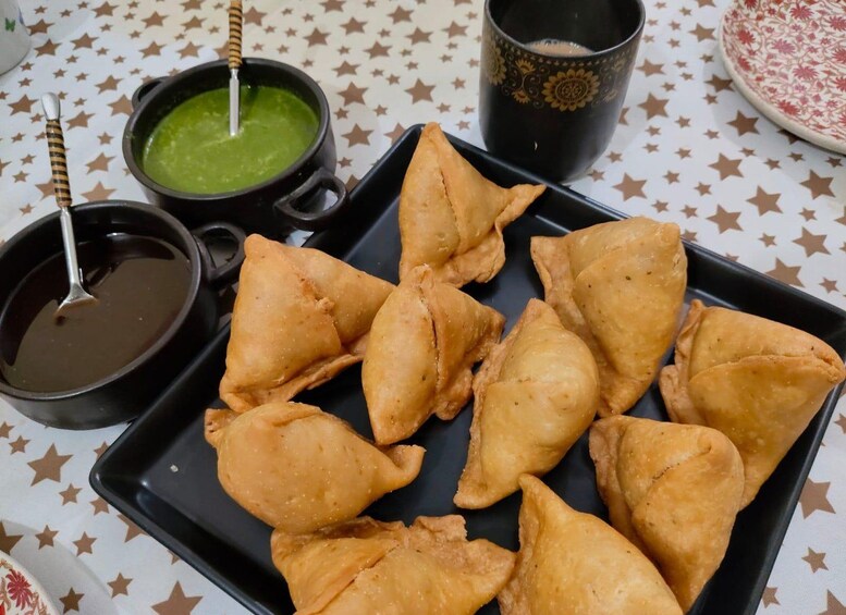 A plate of samosas with two dipping sauces, a mug, and a patterned tablecloth. 3