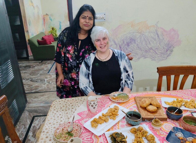 Two people seated at a table with various dishes, including fried snacks and a cup of tea. 4