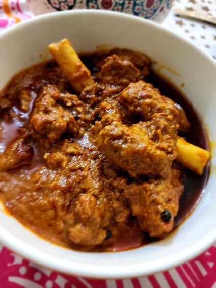 A bowl of meat stew with bones, in a white bowl on a tablecloth. 5