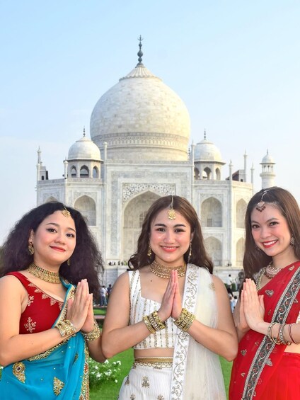 Three women in traditional attire standing in front of the Taj Mahal. 5
