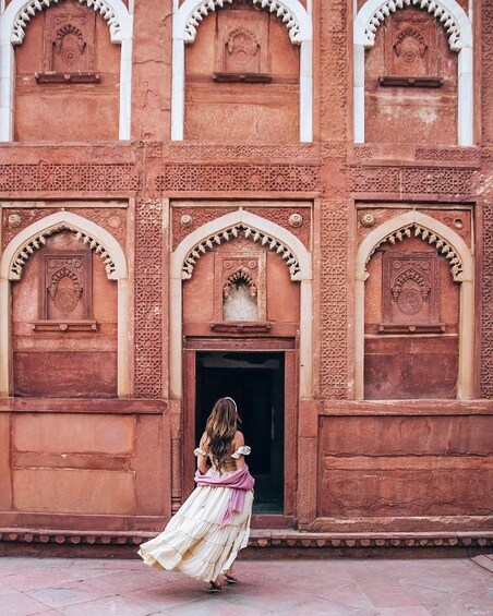 A woman in a flowing dress standing in front of a building with arched windows and intricate carvings. 4