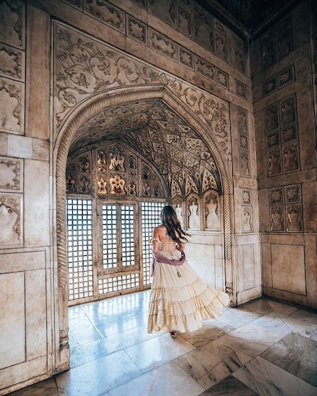 A woman in a flowing dress walking through an ornate hallway with intricate carvings and a large arched doorway. 3