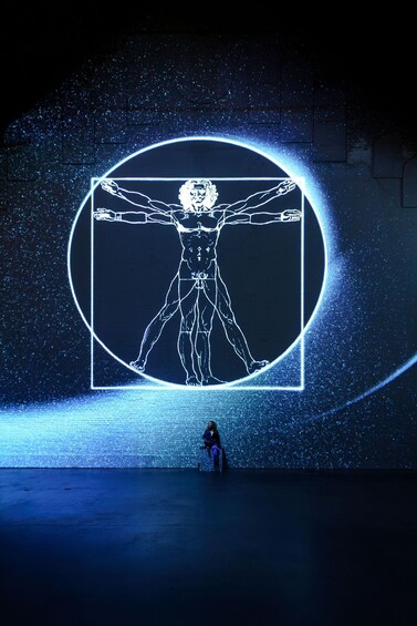 Una persona sentada frente a una gran proyección iluminada de una figura humana. 4