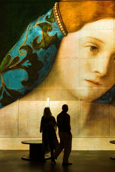 Un mural con un retrato grande de una mujer y dos personas caminando delante. 3