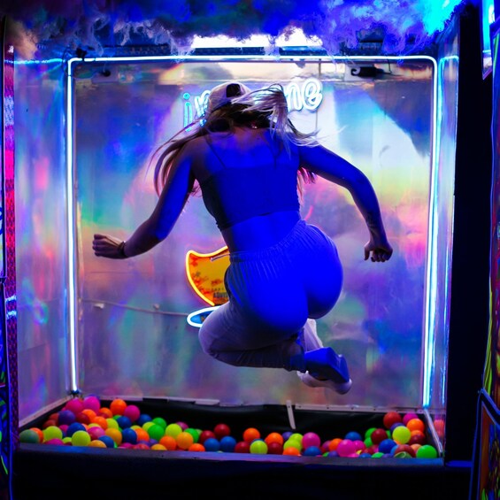A person jumping inside a claw machine filled with colorful balls. 5