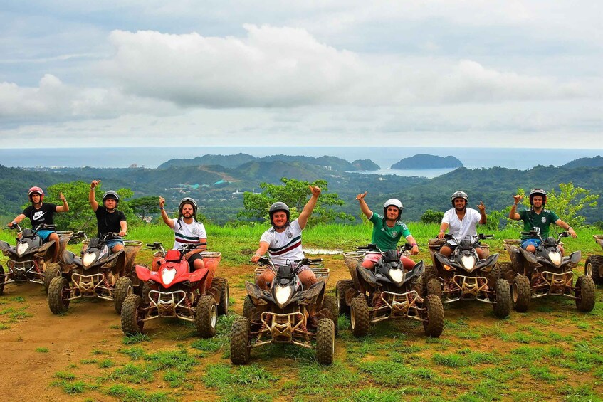 A group of people on ATVs on a dirt path with a scenic view of hills and a body of water in the background. 2