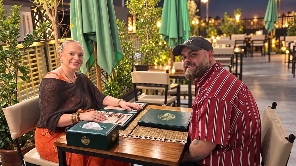 Two people seated at a table with a board game, surrounded by outdoor seating and greenery. 5