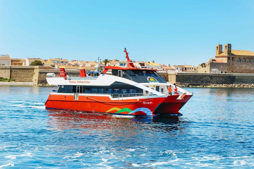 Un ferry rojo y blanco llamado 'Vision Submarine' con un diseño colorido en su lateral, navegando sobre aguas tranquilas. 1