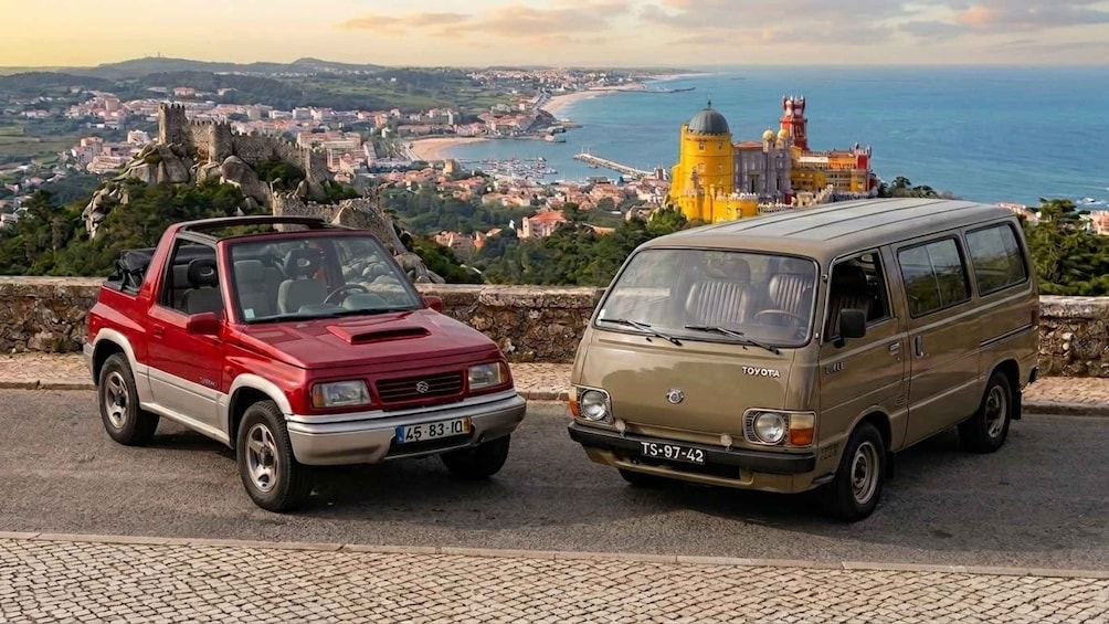 A red and a beige van parked on a cobblestone path with a scenic coastal view in the background. 2