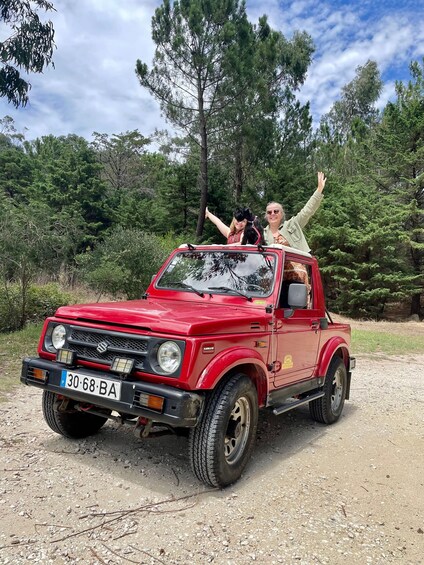 A red Suzuki pickup truck on a dirt road with two people in the back, surrounded by trees. 1