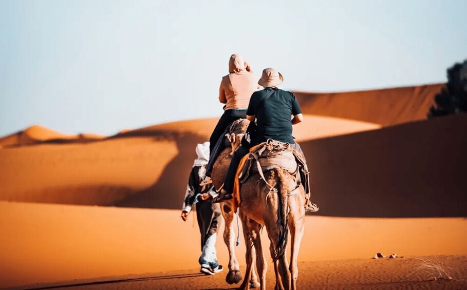 Two people riding a camel in a desert with sand dunes. 3