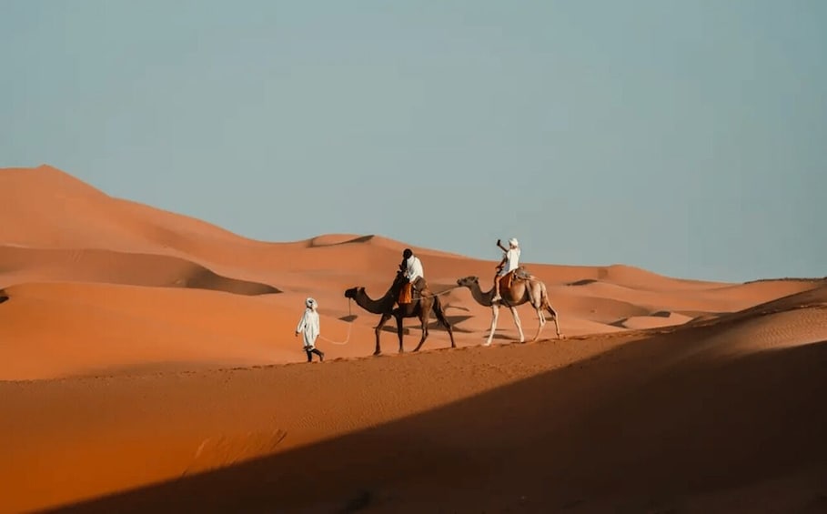 A desert landscape with sand dunes and three camels with riders. 4