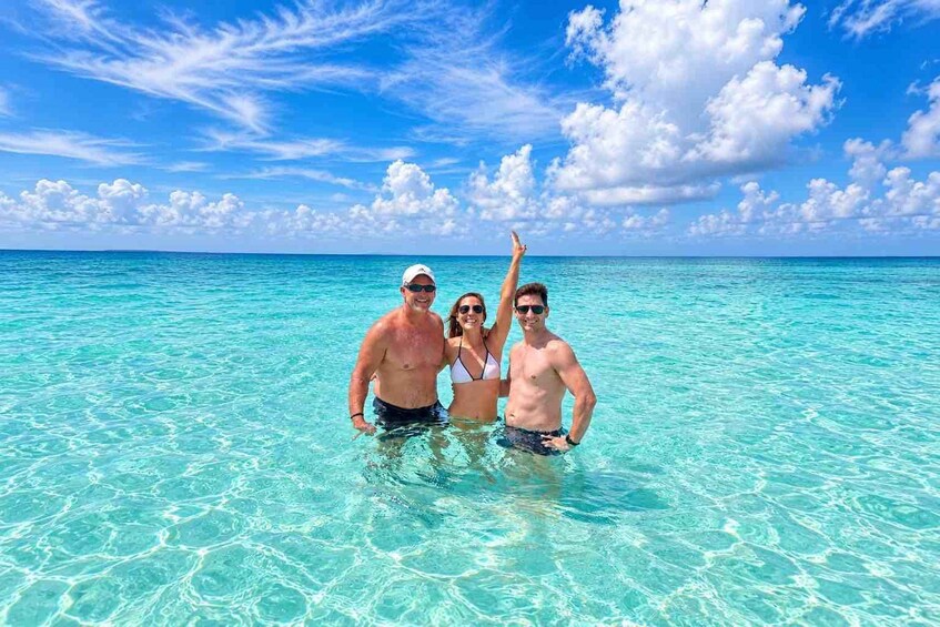 Drie mensen staan in helder turquoise water, met een blauwe lucht en enkele wolken erboven. 5