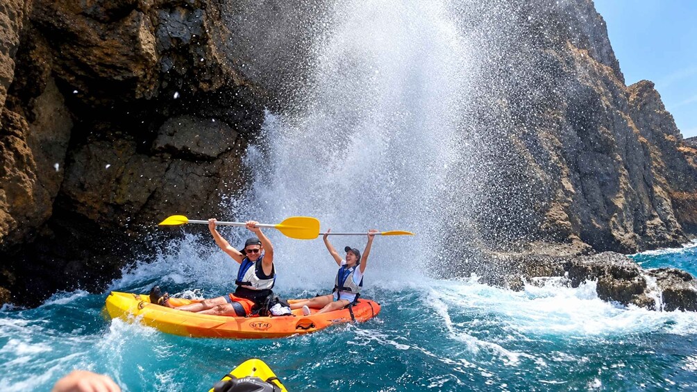 Two people kayaking in rough waters with a rocky cliff in the background. 3