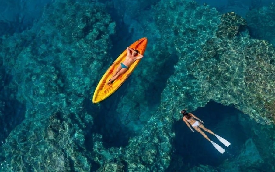 A person kayaking and another person swimming in clear blue water with visible underwater rocks. 1