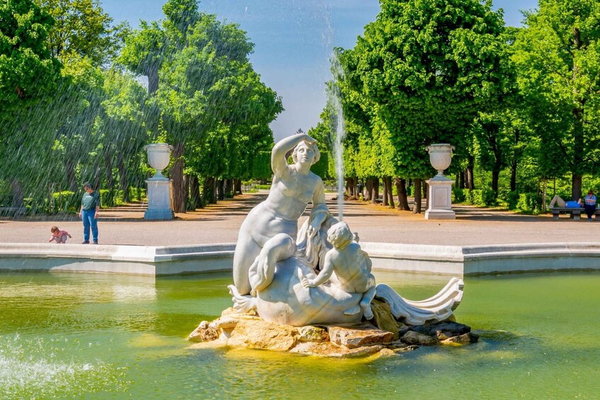 A statue of a woman and child by a fountain in a park. 2