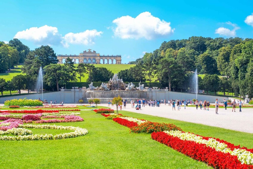 A large garden with a fountain, colorful flower beds, and a grand building in the background. 1